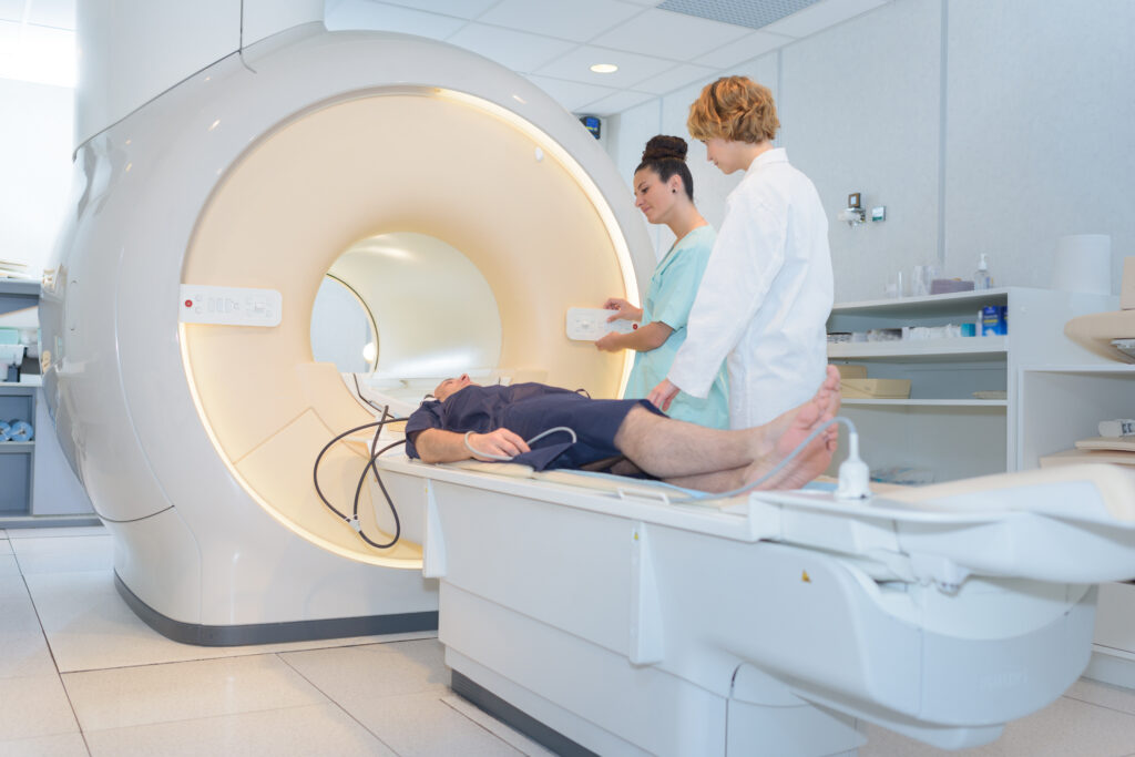 Patient positioned on a CT scanner table while medical staff prepare imaging equipment in a clinical setting