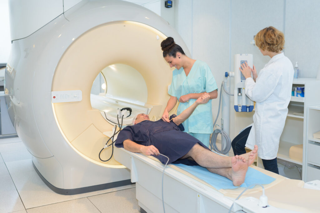 Patient lying on a CT scanner table while medical staff prepare and monitor a diagnostic imaging procedure
