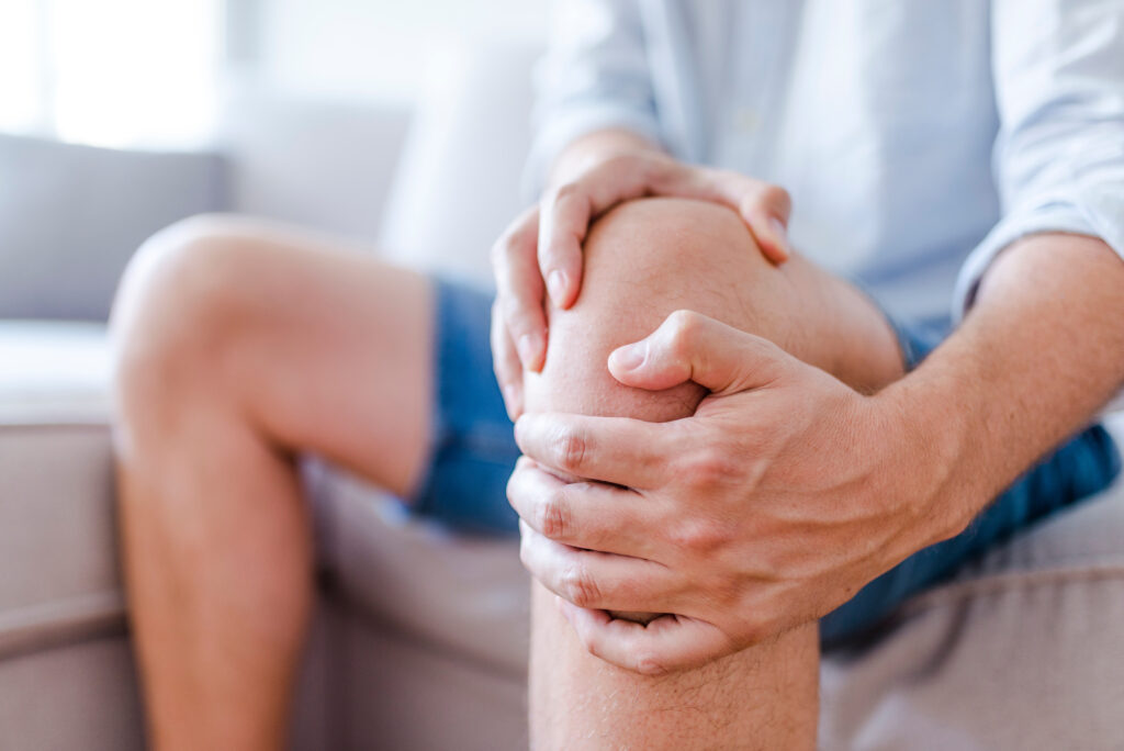 Person holding their knee with both hands, indicating knee pain, joint stiffness, or possible injury