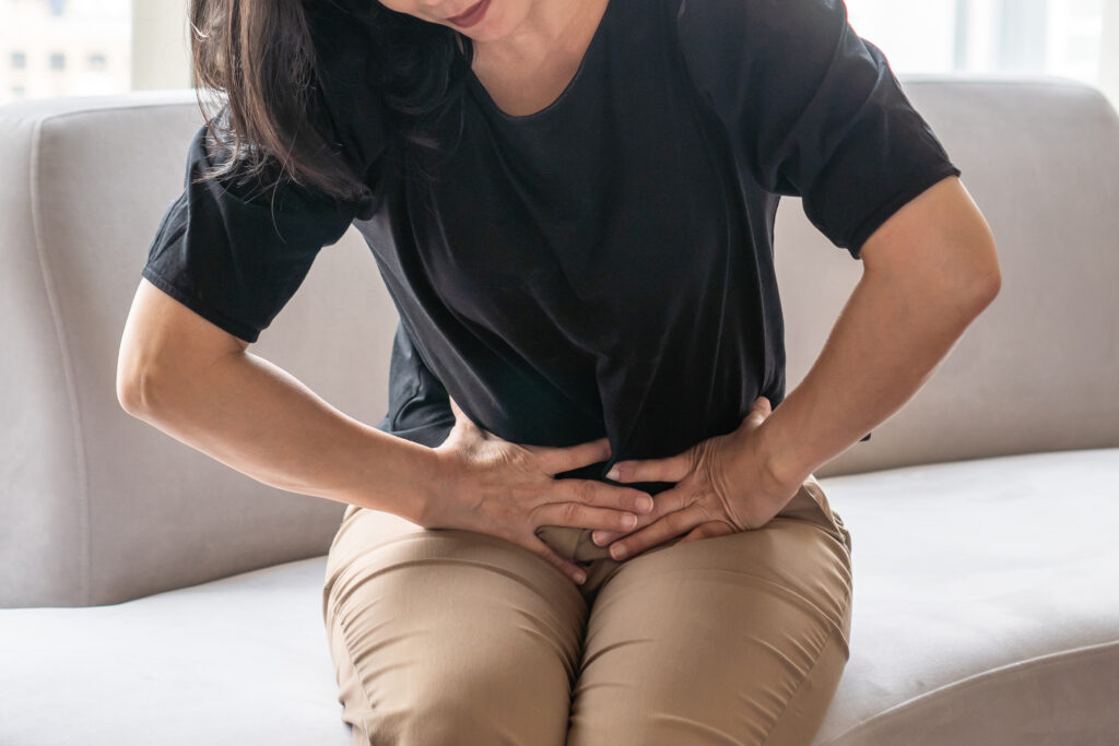 Woman sitting and holding her lower abdomen, indicating abdominal pain or digestive discomfort
