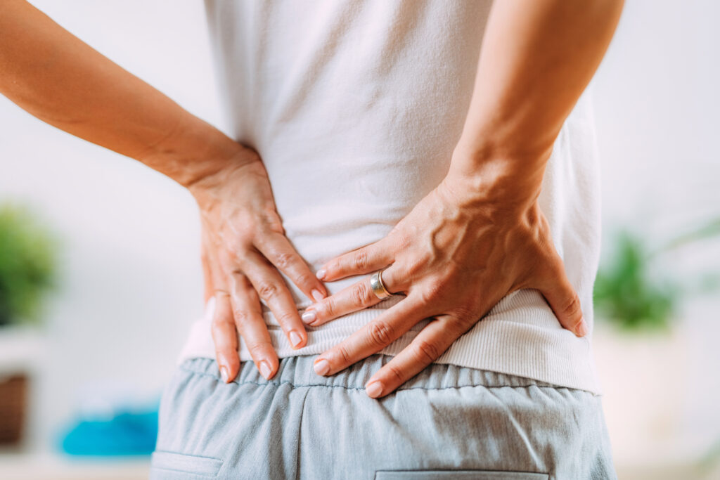Person holding their lower back with both hands, indicating back pain or spinal discomfort