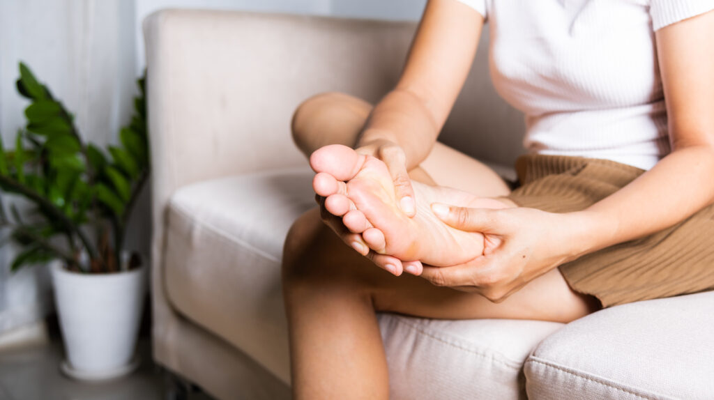 Person sitting on a couch holding the sole of their foot, indicating foot pain or plantar discomfort