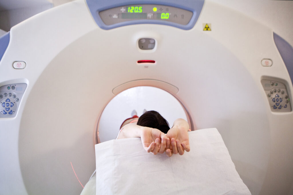Patient lying on a CT scanner table with arms raised, positioned for a medical imaging scan