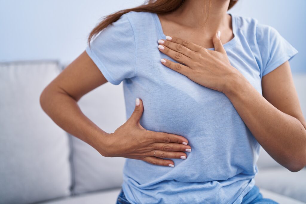 Woman holding her chest and upper abdomen, indicating chest discomfort or possible digestive pain