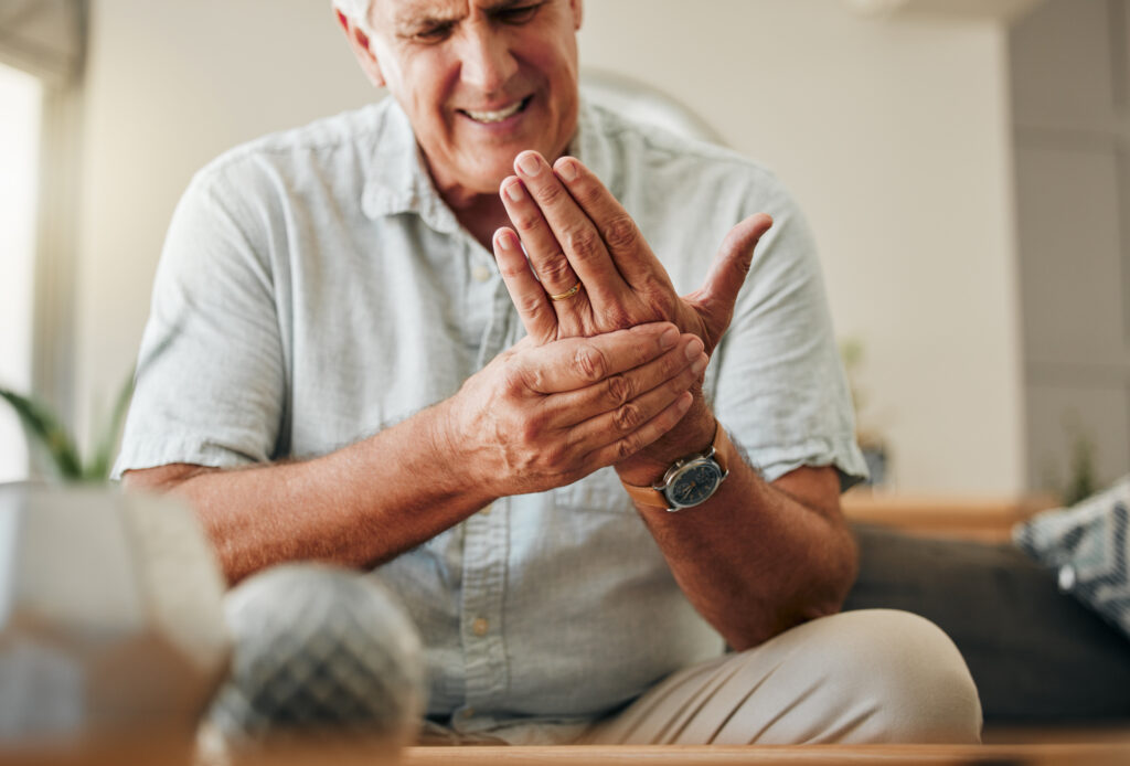 Man holding his hand in pain while sitting indoors, suggesting hand pain or joint stiffness