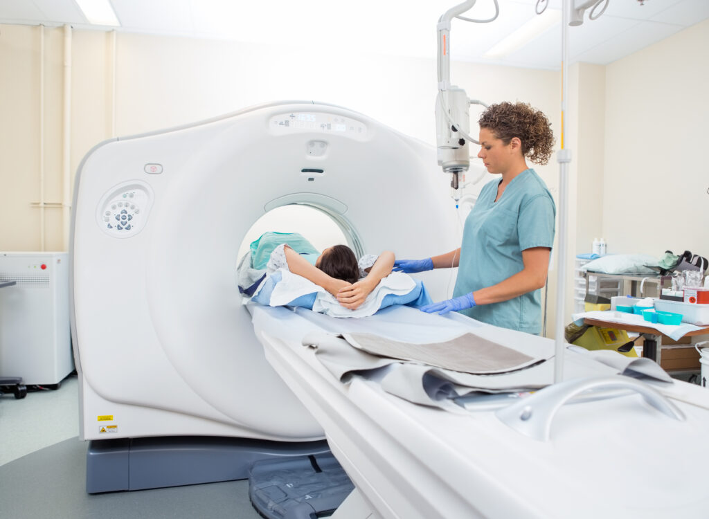 Medical technician assisting a patient on a CT scanner table during a diagnostic imaging procedure